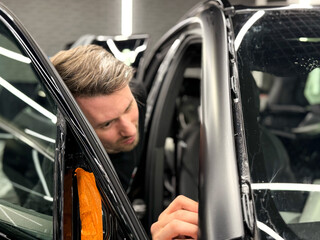 A car wrapping specialist applies a polyurethane film to the car. Detailer smoothes PPF. Car wrapping, detailing, tuning and styling. Selective focus. Car detailing and wrapping workshop. 
