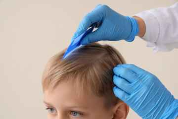 Female doctor combing little boy's hair with pediculosis on beige background, closeup