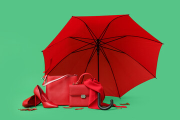 Stylish female handbags, shoes, umbrella and fallen leaves on green background
