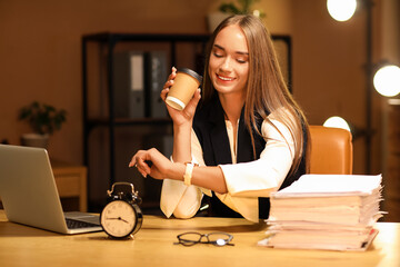 Happy businesswoman with coffee cup and wristwatch meeting deadline in office at night