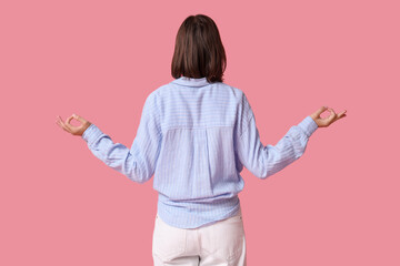 Pretty young woman meditating on pink background, back view