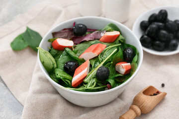 Bowl of salad with crab sticks, spinach, black olives and wooden scoop, closeup