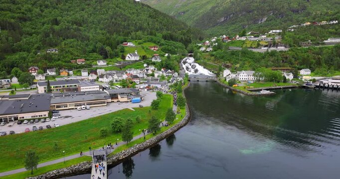View on Hellesylt, a small village in the Sunnylvsfjord, Norway. Captured from a large cruise ship, the scene features a lush green landscape, a waterfall, and serene fjord waters.
