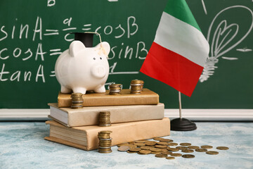 Piggy bank with coins, books and Italian flag on table near blackboard. Student loan concept