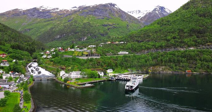 View on Hellesylt, a small village in the Sunnylvsfjord, Norway. Captured from a large cruise ship, the scene features a lush green landscape, a waterfall, and serene fjord waters.