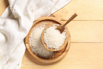 Tray and bowl of raw rice with scoop on wooden background