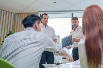 multiracial business people meeting in boardroom,two caucasian man presentation with small solar panel,all discussing and share ideas for a new real estate house project with solar roof