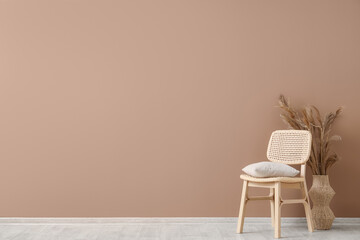 Comfortable wooden chair with cushion and vase of pampas grass near brown wall
