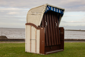 Traditional German wicker beach chair (Strandkorb) standing on green grass, closed and striped canopy up, symbolizing leisure, summer, and classic European outdoor design.