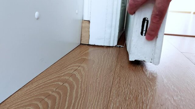 Hands inspect a floor-mounted door lock-fingers test the latch and alignment, capturing a close-up moment of tactile focus and quiet home security attention
