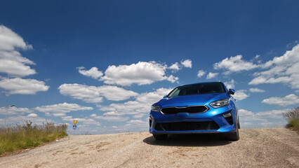 Low-angle view of a blue car parked on a roadway during summertime, with puffy clouds in the sky- travel and road trip concept.