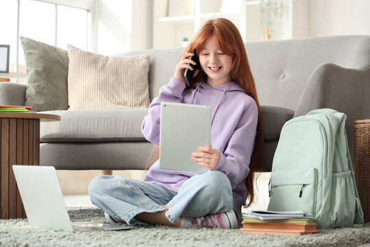 Cute ginger girl with backpack, modern laptop and tablet computer talking by phone at home - Powered by Adobe