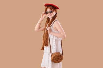 Cute ginger girl in stylish dress and beret on beige background