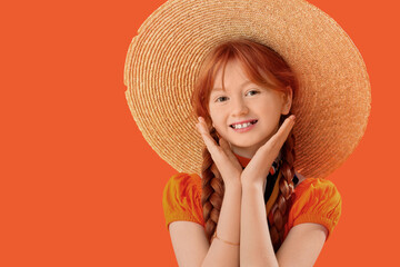 Cute ginger girl in stylish dress and hat on orange background