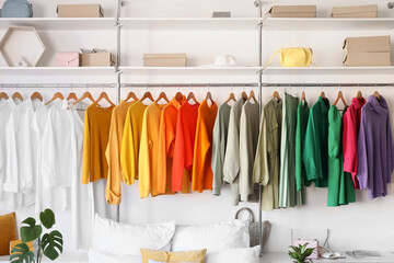 Stylish wardrobe with colorful clothes near bed in light bedroom