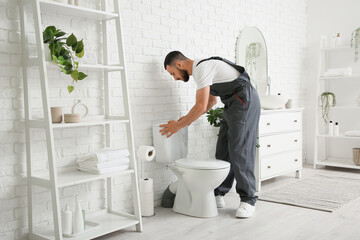 Male plumber repairing toilet tank in light restroom