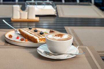 Cup of coffee, a piece of honey cake on a table in a sidewalk cafe.