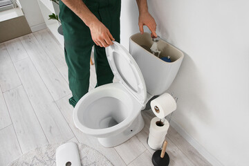 Male plumber repairing toilet in restroom, closeup