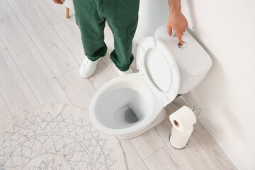 Male plumber flushing fixed toilet in restroom, top view