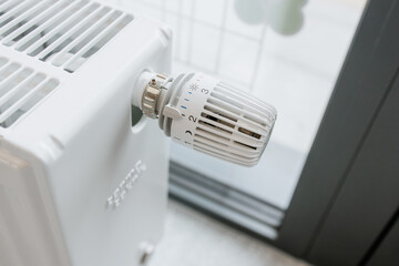 Close-up of a white radiator with a temperature control thermostat valve in a modern interior setting, showing heating regulation and energy efficiency
