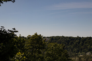A scenic view of a distant historic building nestled among dense green forested hills under a clear...