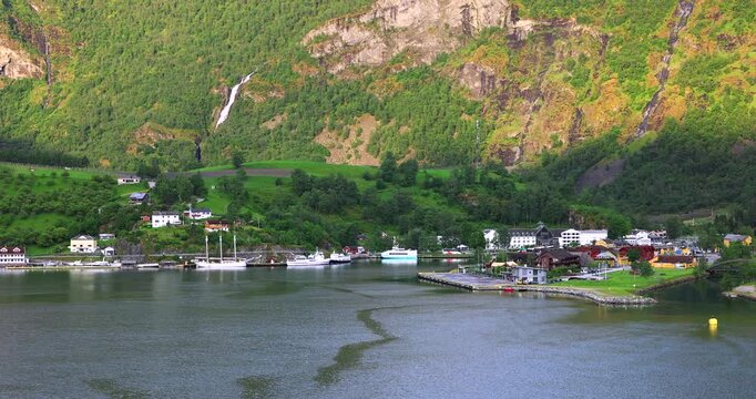 Morning arrival to Flаm, a cruise ship slowly sails the calm fjord waters, surrounded by green hills, cozy houses, and a peaceful Nordic landscape.