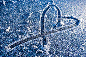 Heart shape drawn in frost on a cold winter morning with small stones on a gray surface