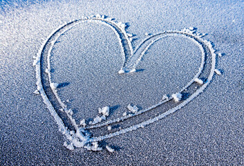 Heart shape drawn in frost on a cold winter morning with small stones on a gray surface