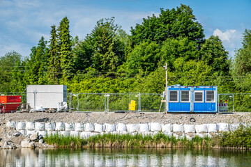 Construction site along a riverbank featuring portable structures and protective vegetation in a...