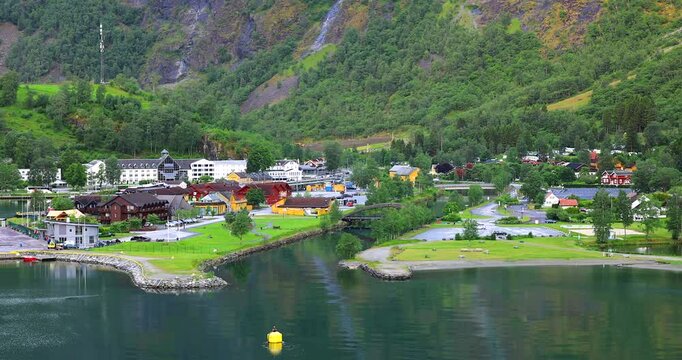 Evening departure from Flаm, a cruise ship slowly sails the calm fjord waters, surrounded by green hills, cozy houses, and a peaceful Nordic landscape.