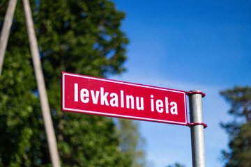 Close-up of a red Latvian street sign labeled “Ievkalnu iela,” captured outdoors against a...