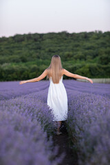 Beautiful young woman in white dress with bouquet of lavender flowers on lavender field