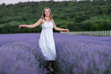 Beautiful young woman in white dress with bouquet of lavender flowers on lavender field