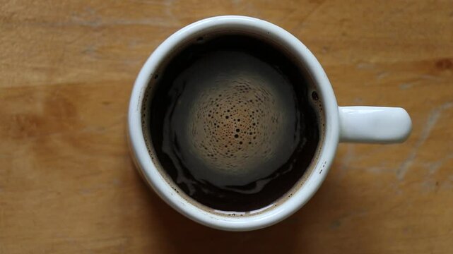 Coffee swirls in white cup on wooden table top, coffee