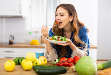 Young woman in blue silk robe enjoying vegetable salad in kitchen