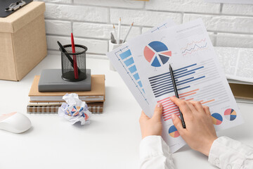 Woman with pen and business charts working at table in office, closeup