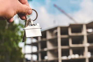 Hand Holding House Keys Against New Building Construction, Real Estate Dreams