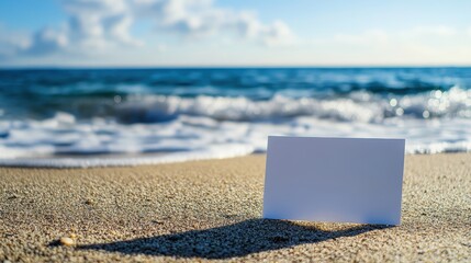 White card on beach sand with blurred sea and sky backdrop. Perfect for mockups, promotions or travel-themed creative projects.