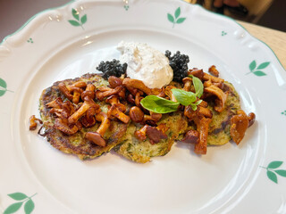 Vegan Zucchini Pancakes with Chanterelle Mushrooms, Plant-Based Black Caviar, and Tofu Basil Sauce on Table. Modern Vegan Cuisine Concept. Handheld Phone Photo, Selective Focus, Non-AI