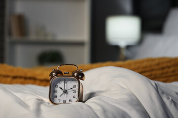 Alarm clock on bed with soft blanket in bedroom, closeup