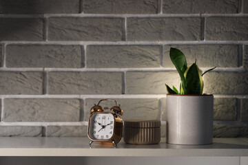 Alarm clock, glowing lamp and houseplant on shelving unit in bedroom, closeup