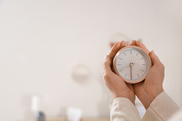 Female hands holding alarm clock in bedroom, closeup