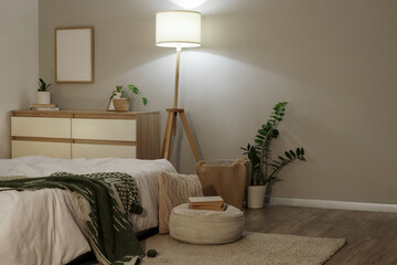 Interior of stylish bedroom with cozy bed and glowing standard lamp at evening
