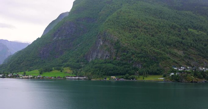 Majestic green cliffs and deep blue fjord waters under cloudy skies, filmed from a cruise ship sailing through the breathtaking landscapes of Norway fjords.