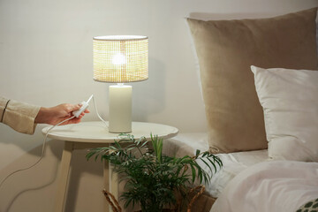 Woman turning off glowing lamp on bedside table in bedroom at evening, closeup