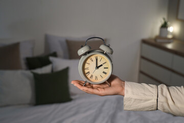 Female hand holding alarm clock in bedroom, closeup