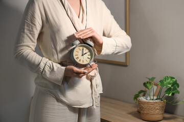 Young woman holding alarm clock in bedroom
