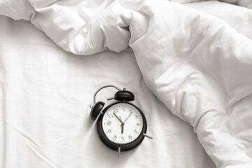Alarm clock on bed with crumpled blanket, top view