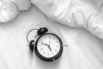 Alarm clock on bed with crumpled blanket, top view