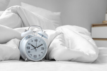 Alarm clock on bed with crumpled blanket, closeup